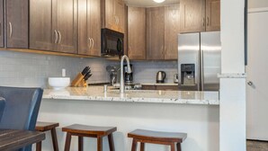Une cuisine moderne avec des meubles en bois, un réfrigérateur en acier inoxydable, une machine à café et un évier.