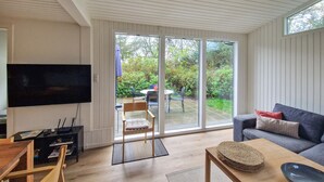 A modern living room with a flat-screen TV, a sofa, a coffee table, and a sliding glass door leading to an outdoor patio with a table and chairs. - Beautiful home in Hjørring with WiFi (Hjørring)