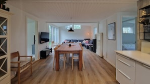 A spacious living area with a wooden dining table, a sofa, and a television mounted on the wall. - Beautiful home in Hjørring with WiFi (Hjørring)