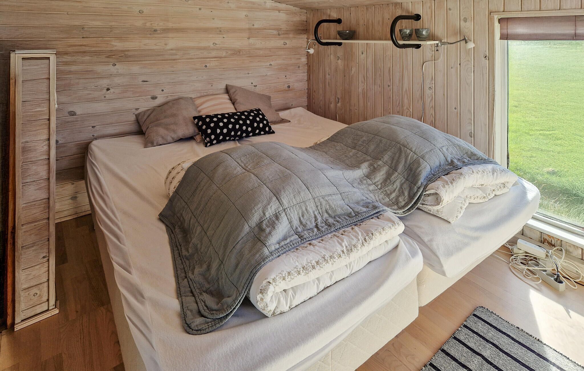 Un lit avec une couette grise, plusieurs oreillers et un mur en bois.