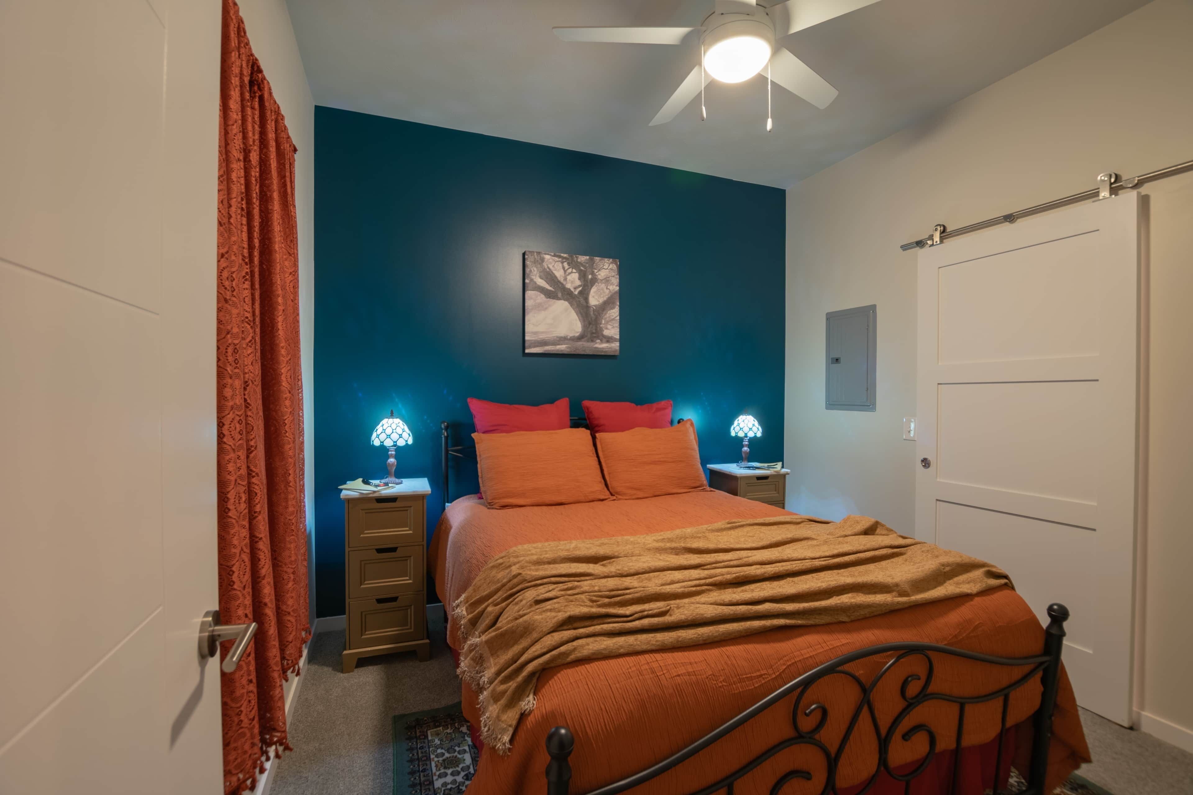 Une chambre à coucher comprenant un lit, deux tables de chevet, une commode, un ventilateur de plafond et une porte.