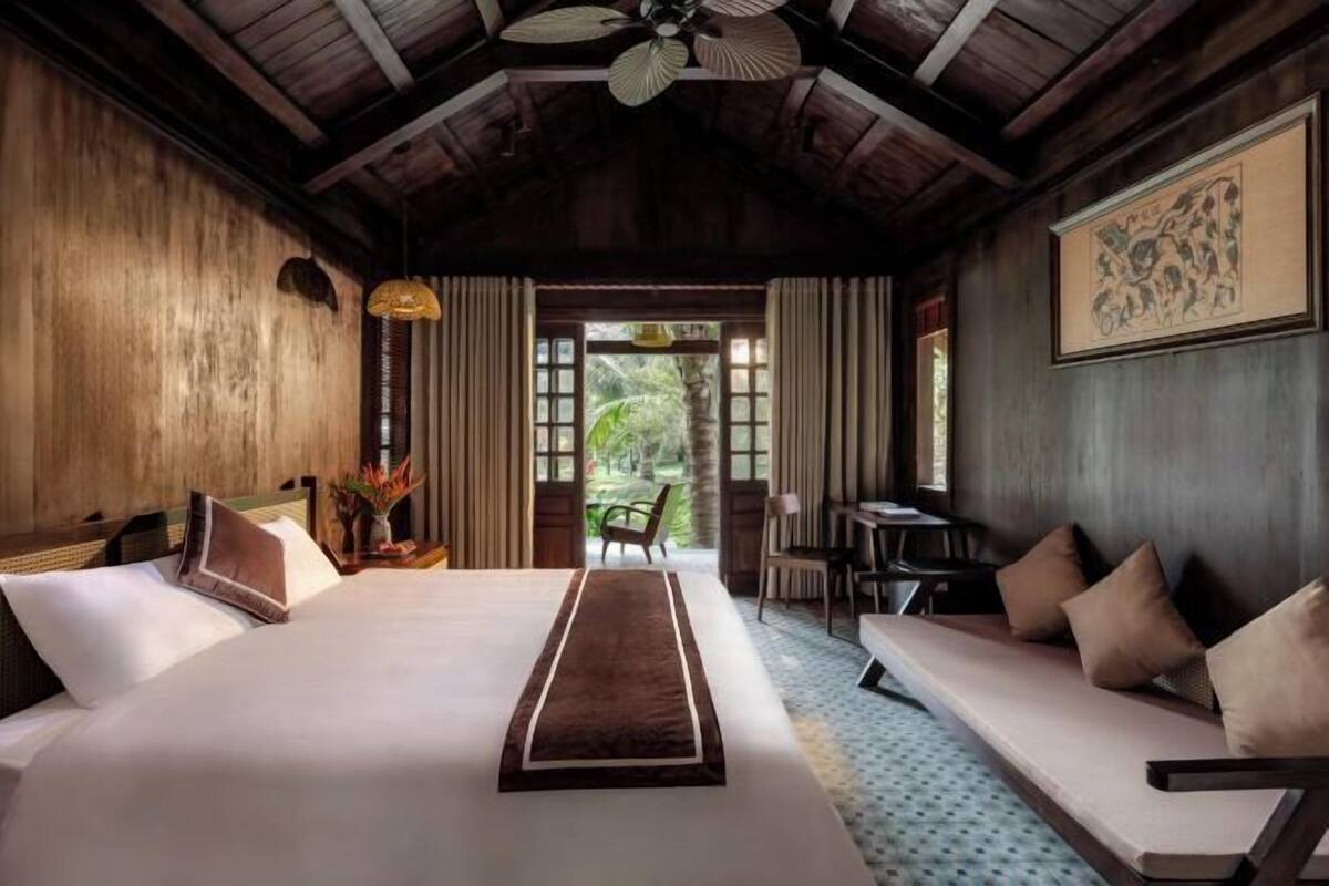 A hotel room with a large bed, a sofa, a dining table, and a ceiling fan.