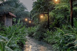 Ein schmaler Wasserweg, gesäumt von üppiger Vegetation und traditionellen Häusern mit Strohdächern, beleuchtet durch dezentes Licht.