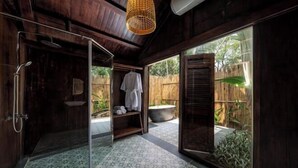 Un baño con ducha, un estante con toallas y vistas a un jardín a través de amplias ventanas.