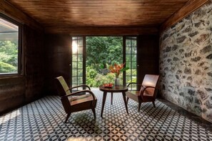 Una habitación con pared de piedra, suelo estampado y vistas al verdor a través de amplios ventanales.