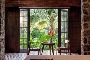 A room with a large window, a table with chairs, and a view of tropical plants. - Nature Garden Ecolodge Ninh Binh (Hoa Lu District)