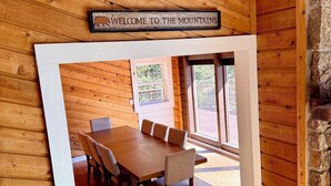 Un interior de madera con una mesa y sillas de comedor, un letrero que dice 'Welcome to the Mountains' y una pared de piedra.