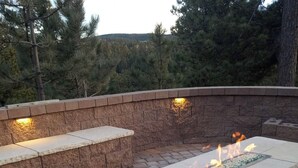 Una estructura de fuego de piedra con tapa de vidrio y escalones, rodeada por un muro de piedra y un área pavimentada.
