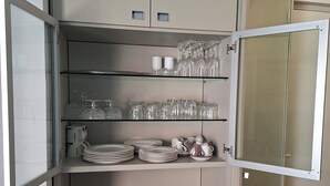 A kitchen with open cabinets displaying glassware, plates, and a coffee maker. - Quiet apt, A/C, 10mn walk to beaches, large terrace w/view over old town (Menton)
