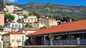 A hillside residential area with terracotta-tiled roofs, a mix of building styles, and a mountain backdrop. - Quiet apt, A/C, 10mn walk to beaches, large terrace w/view over old town (Menton)
