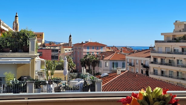 A coastal cityscape with a mix of traditional and modern buildings, a prominent church tower, and a clear view of the sea. - Quiet apt, A/C, 10mn walk to beaches, large terrace w/view over old town (Menton)