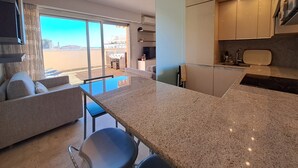 A modern kitchen with a large island, a dining area with a table and chairs, and a view of the beach through large sliding doors. - Quiet apt, A/C, 10mn walk to beaches, large terrace w/view over old town (Menton)