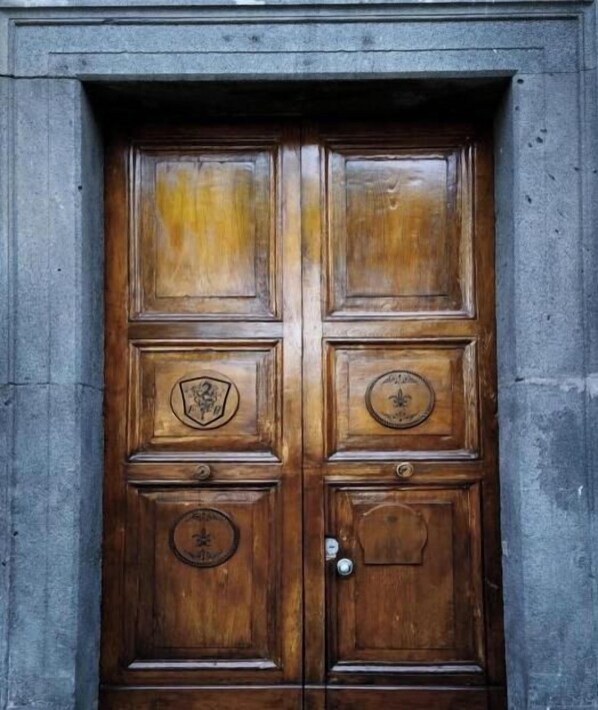 A wooden double door with a metal handle and a circular emblem on the lower right panel. - Hotel Villa Nunziante  (Scafati)