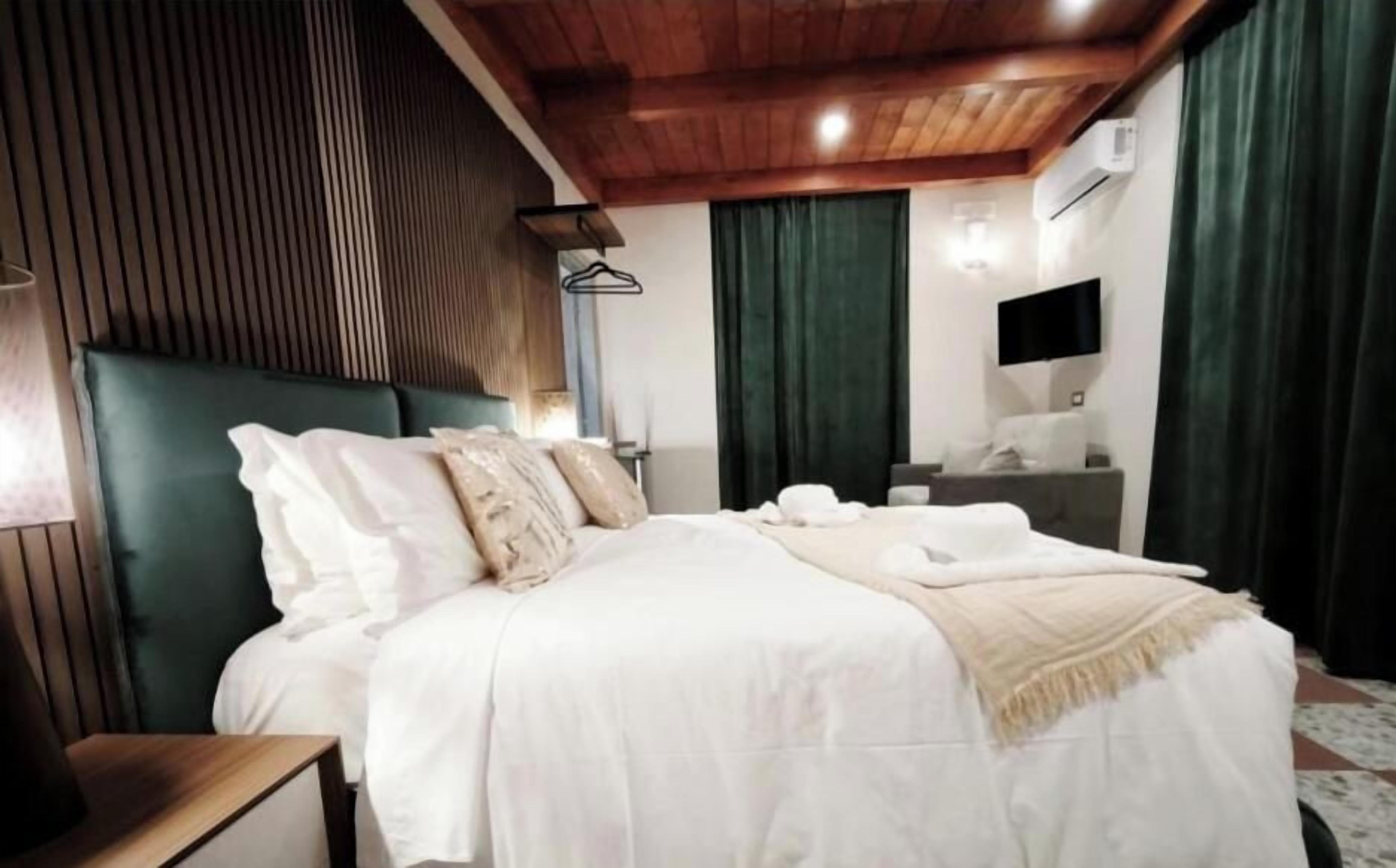 Une chambre à coucher avec un grand lit, une table de chevet, une commode, un téléviseur fixé au mur et une fenêtre avec des rideaux.