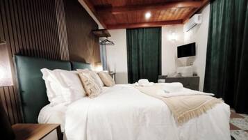 Une chambre à coucher avec un grand lit, une table de chevet, une commode, un téléviseur fixé au mur et une fenêtre avec des rideaux.