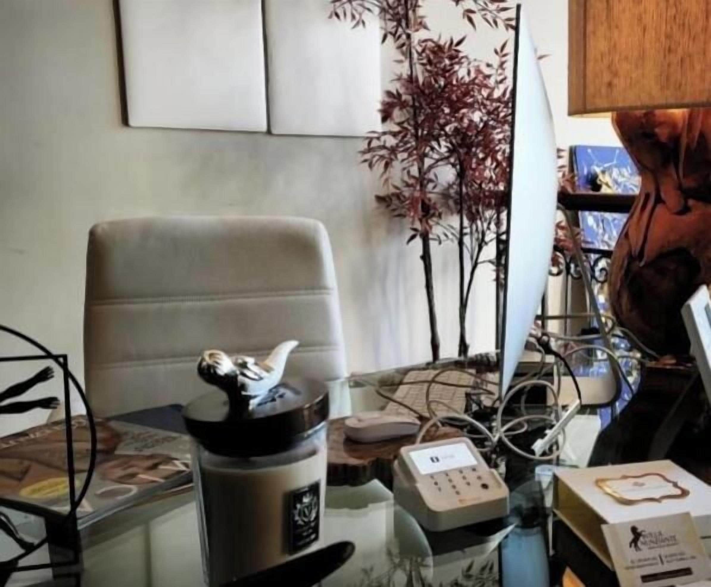 A room with a glass table, a chair, a water bottle, a clock, and a decorative plant.