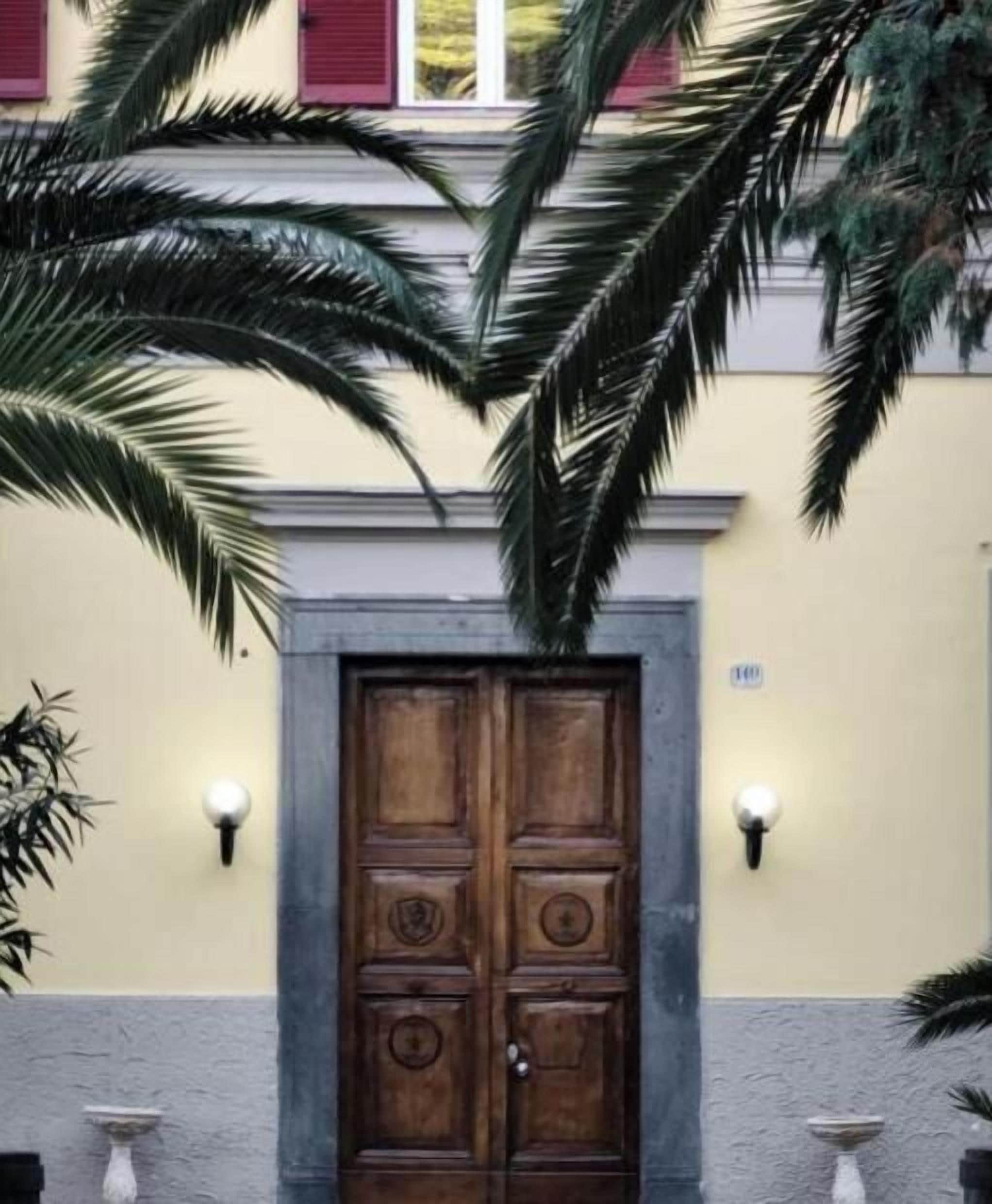 A wooden double door with a decorative design, flanked by wall-mounted light fixtures, and a number plaque above the door.
