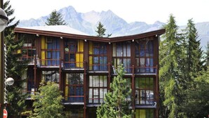 A multi-story building with balconies, surrounded by trees and mountains in the background. - Quiet Mezzanine Duplex for 6 People (Bourg-Saint-Maurice)