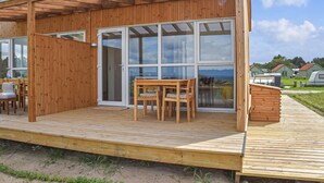 A wooden cabin with a covered patio, large sliding glass doors, and a view of the landscape. - Nice home in Hanstholm with house sea view (Hanstholm)