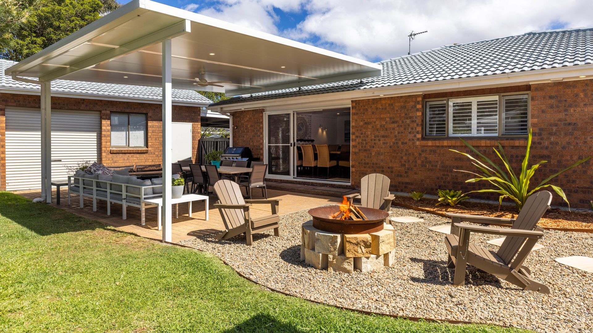 A residential backyard with a covered patio, outdoor seating, a fire pit, and a barbecue area.