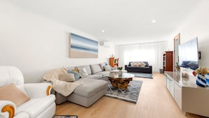 Una sala de estar moderna con un sofá seccional gris, un sillón blanco, una mesa de centro y un cuadro grande de una playa.