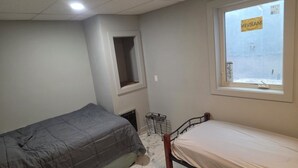 A small, sparsely furnished room with two single beds, a window with a view, and a small window above the door. - Man cave 2.0 (Circle)