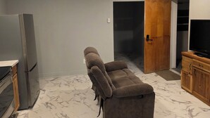 A living room with a sofa, a TV, a wooden cabinet, and a marble floor. - Man cave 2.0 (Circle)
