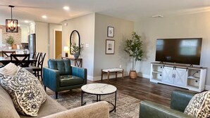 A living room with a sofa, armchair, coffee table, TV stand, and a dining area with chairs and a table. - Peaceful Home near Historic Strasburg (Lancaster)