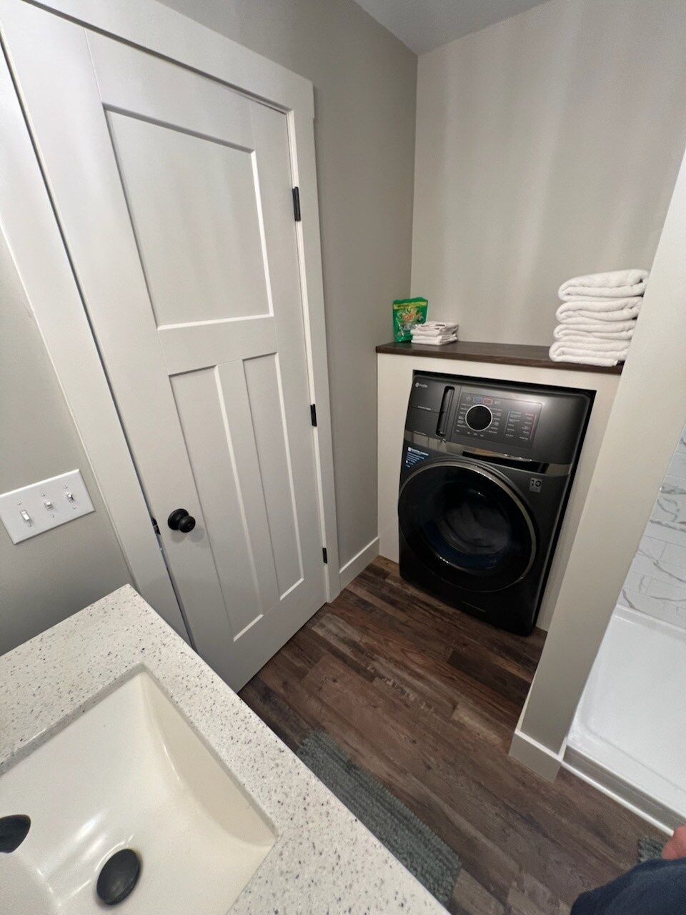 Een kleine wasruimte met een wasmachine, een deur en een aanrecht met handdoeken.