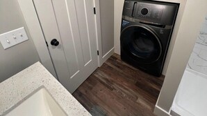 A compact laundry room with a washing machine, a door, and a countertop with towels. - Peaceful Home near Historic Strasburg (Lancaster)