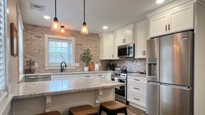 A modern kitchen with white cabinets, stainless steel appliances, a granite countertop, and a brick accent wall. - Peaceful Home near Historic Strasburg (Lancaster)