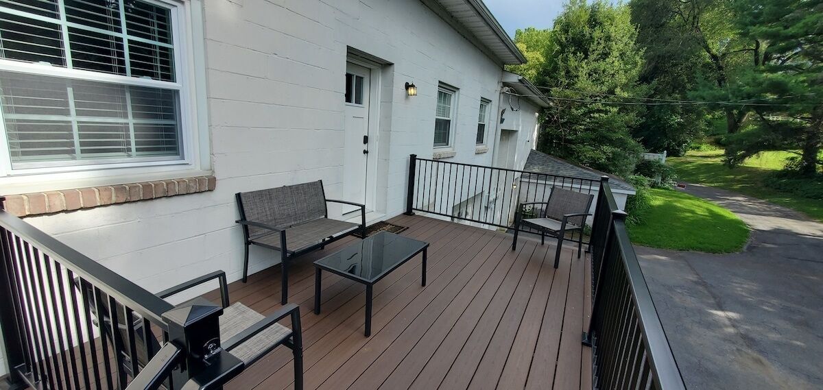 Eine überdachte Terrasse mit Gartenmöbeln, ein weißes Gebäude mit einem Fenster und eine grüne Rasenfläche.