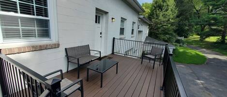 Eine überdachte Terrasse mit Gartenmöbeln, ein weißes Gebäude mit einem Fenster und eine grüne Rasenfläche.