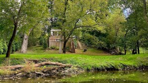 A serene park with a pond, lush greenery, and a wooden structure in the background.