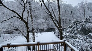 A snow-covered deck with a wooden railing, a bench, and a chair.