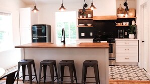 A modern kitchen with a central island, bar stools, a refrigerator, and a coffee machine.