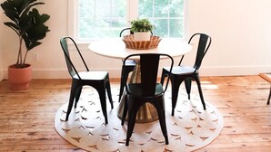 A dining area with a round table, four chairs, a hanging light fixture, a large window, and a potted plant.