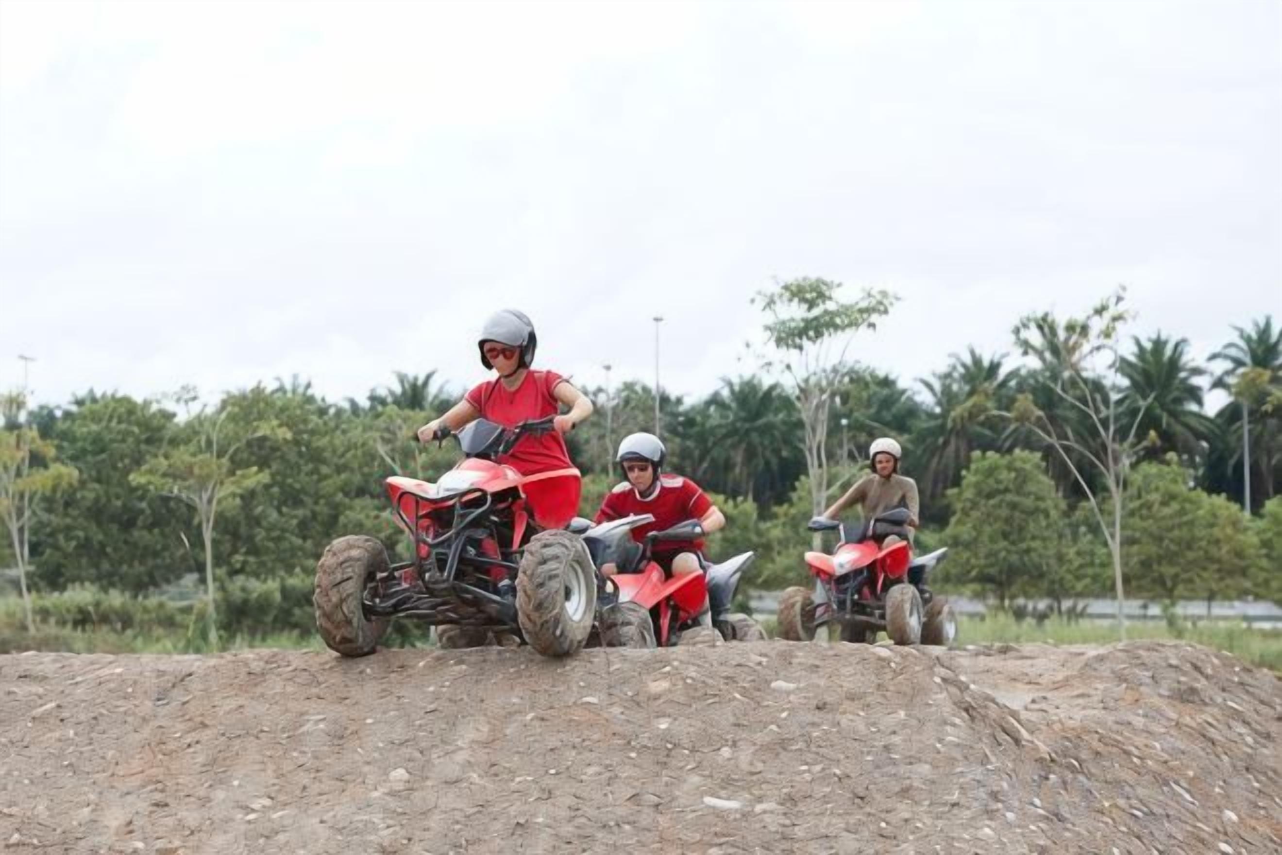 Three people on red ATVs on a dirt mound with trees in the background.