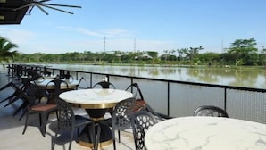 Un espace extérieur aménagé avec des tables et des chaises, offrant une vue sur une étendue d’eau paisible et une végétation luxuriante.