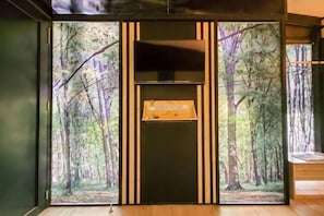 Une pièce dotée d’une grande fenêtre, d’une armoire en bois et d’un tableau représentant une forêt.