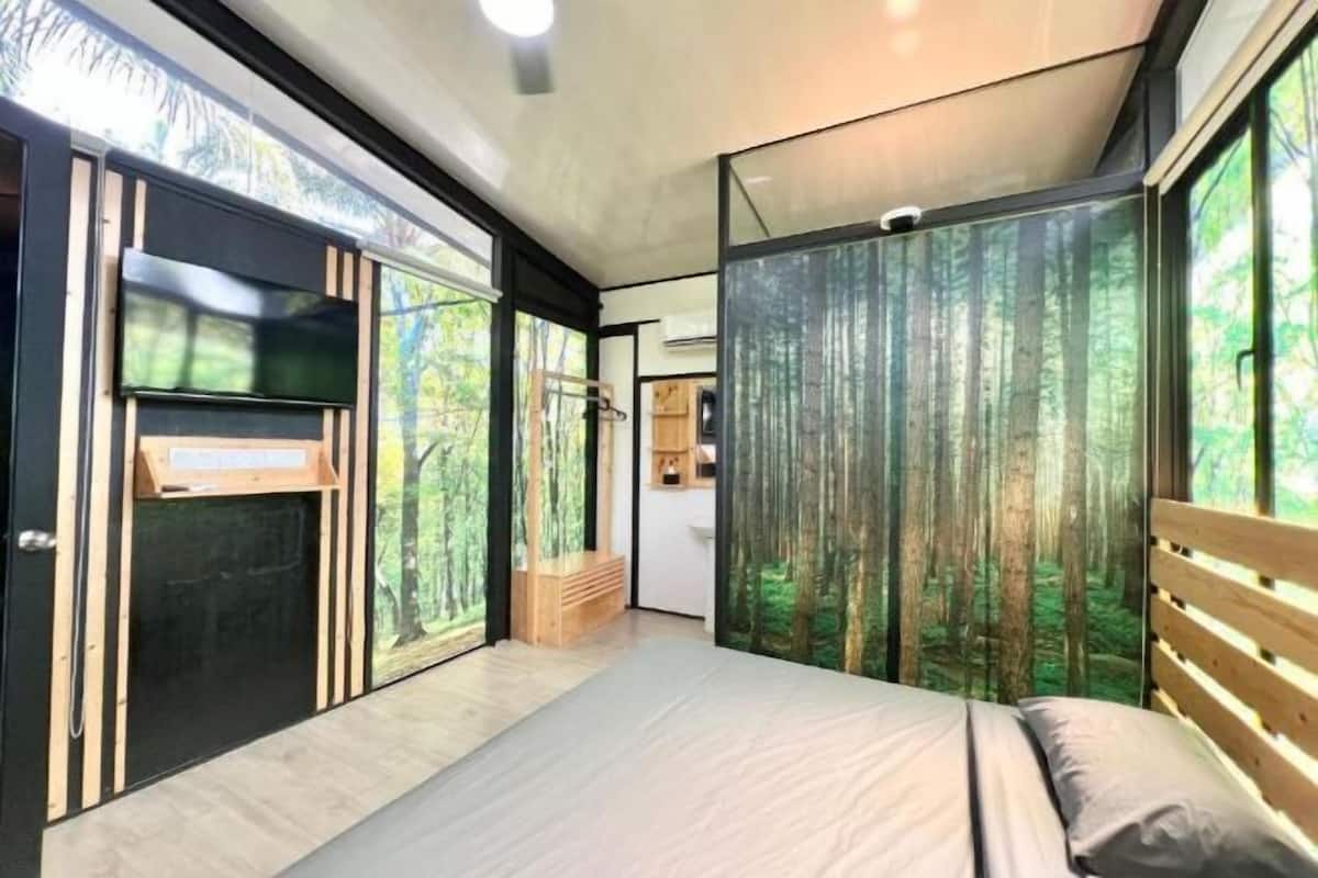 Un dormitorio moderno con una cama grande, un banco de madera y vistas a un bosque a través de un panel de vidrio.