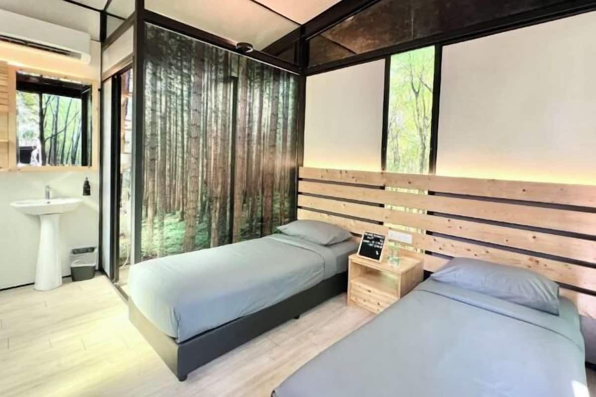 Un dormitorio moderno con dos camas, una mesita de noche, un lavabo blanco y una ventana con vistas a árboles.