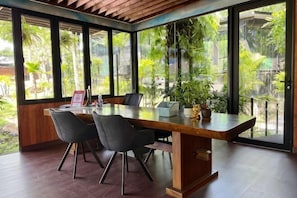 Un coin repas avec une table en bois, quatre chaises et une vue sur la verdure grâce à de grandes fenêtres.