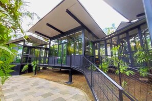 Un bâtiment moderne doté de grandes fenêtres en verre, d’une allée couverte et entouré de verdure.
