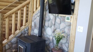 L’intérieur d’une cabane en rondins, avec un mur en pierre, un escalier en bois, un poêle à bois noir, un téléviseur fixé au mur et une petite statue d’ours.
