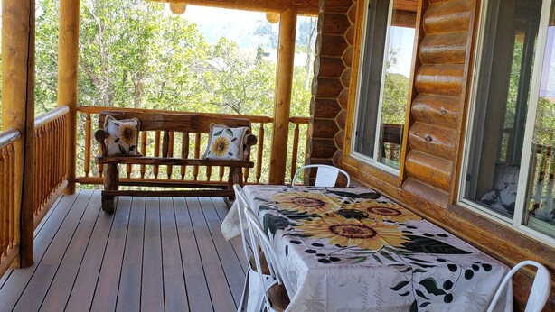 Une terrasse en bois avec une table et des chaises, un banc et un luminaire suspendu.