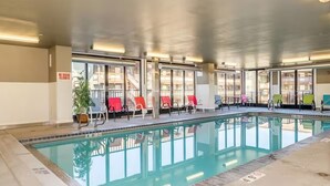Une piscine intérieure à l’eau claire, entourée de murs de verre et agrémentée de nombreuses chaises longues colorées.
