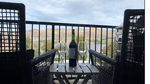 Un balcon avec une table, deux verres à vin et une bouteille de vin.