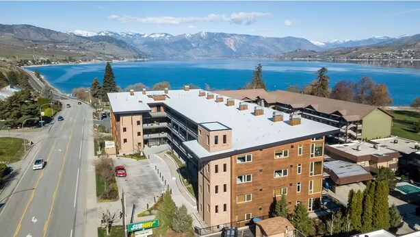 Un bâtiment moderne à plusieurs étages, doté d’un toit plat et offrant une vue sur un lac et des montagnes en arrière-plan.