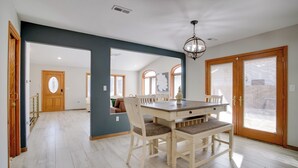 Ein Essbereich mit Holztisch und -stühlen, einem Kronleuchter und Blick auf das Wohnzimmer durch einen offenen Durchgang.